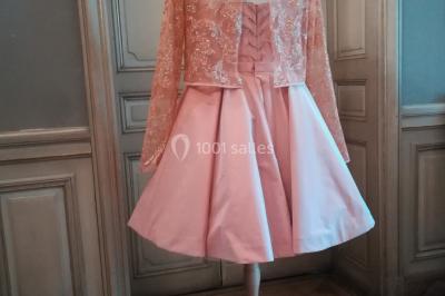 Mannequin vêtu d'une robe en dentelle blanche avec un voile noir couvrant la tête, devant une porte en bois clair.