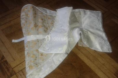 Mannequin vêtu d'une robe en dentelle blanche avec un voile noir couvrant la tête, devant une porte en bois clair.