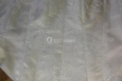 Mannequin vêtu d'une robe en dentelle blanche avec un voile noir couvrant la tête, devant une porte en bois clair.