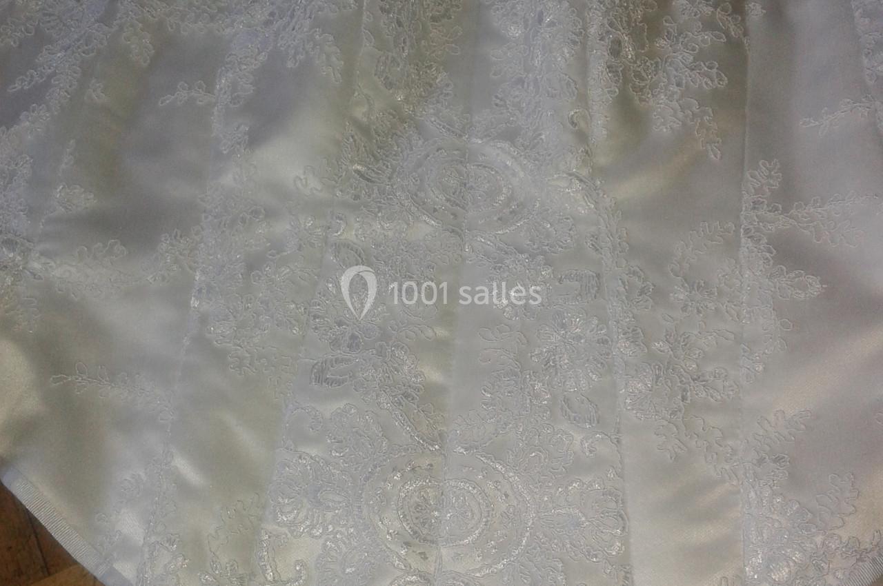 Corset blanc en satin orné de dentelle délicate, posé sur un sol en parquet clair.