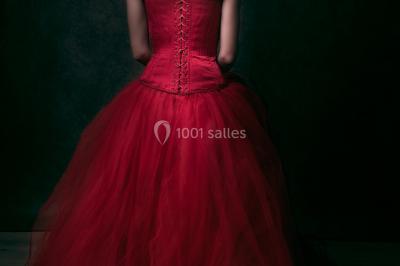 Mannequin vêtu d'une robe en dentelle blanche avec un voile noir couvrant la tête, devant une porte en bois clair.