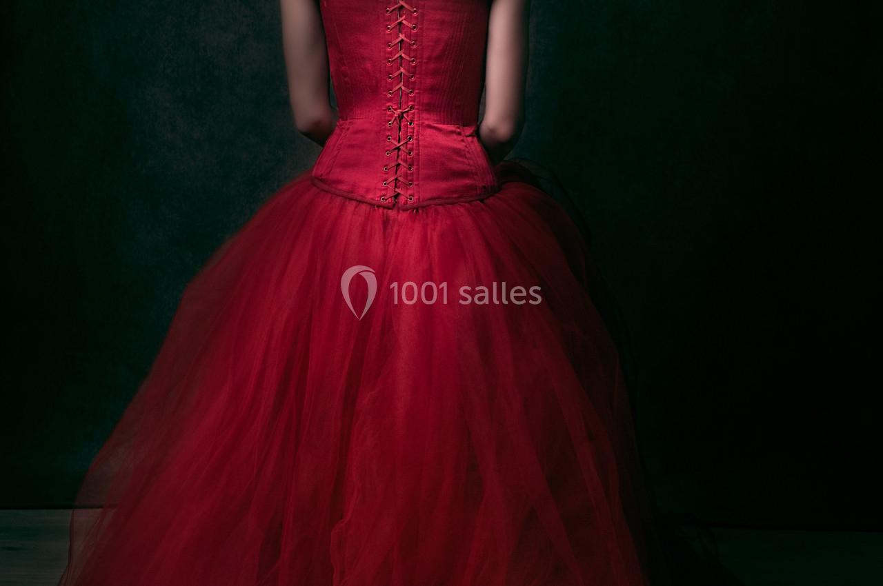 Femme de dos portant une robe rouge corsetée avec une jupe en tulle, coiffée d'une fleur assortie dans les cheveux.