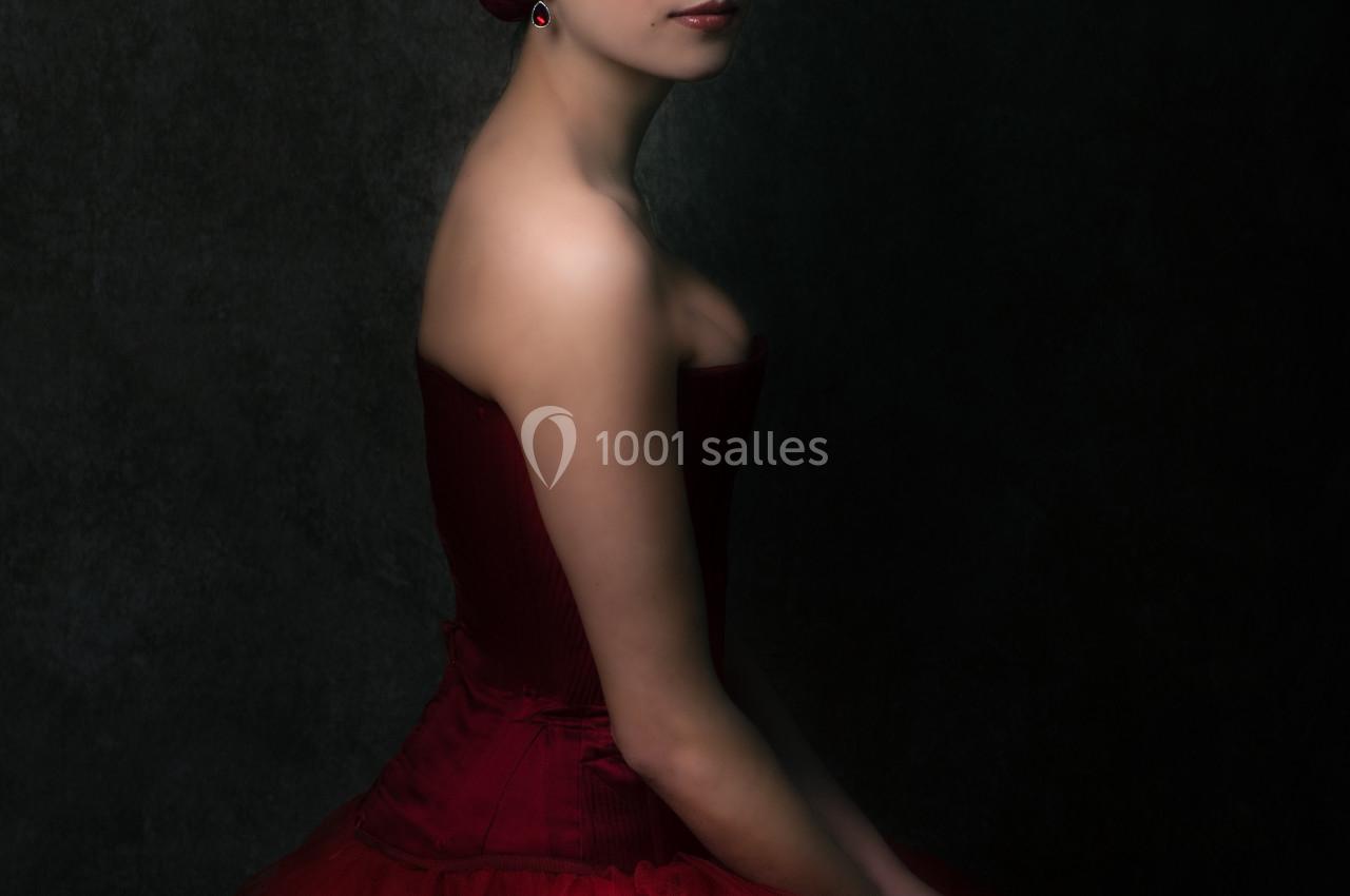 Femme en robe rouge élégante, assise de profil dans un éclairage tamisé sur fond sombre.