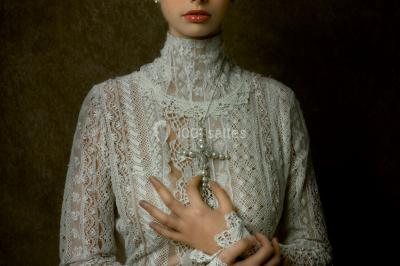 Mannequin vêtu d'une robe en dentelle blanche avec un voile noir couvrant la tête, devant une porte en bois clair.