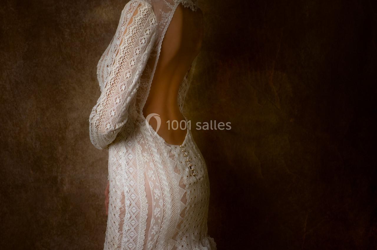 Femme portant une robe de mariée en dentelle avec un dos ouvert, posant devant un fond sombre.