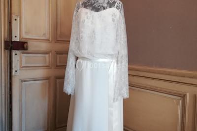 Mannequin vêtu d'une robe en dentelle blanche avec un voile noir couvrant la tête, devant une porte en bois clair.