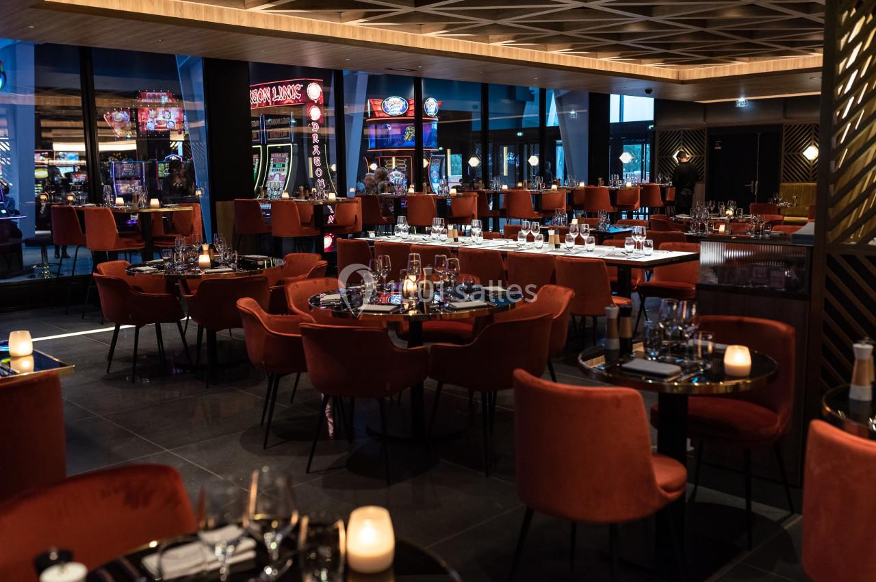 Salle de restaurant élégante avec des tables dressées, des chaises rouges et un éclairage tamisé, vue sur des machines à…