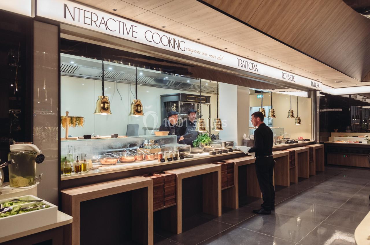 Un homme commande devant un comptoir de cuisine interactive avec des chefs préparant des plats en arrière-plan.