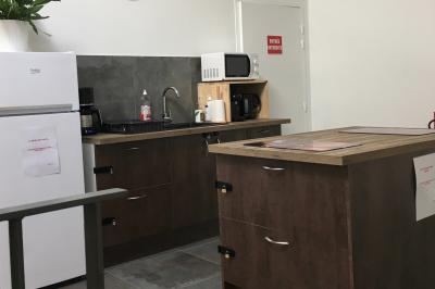 Cuisine équipée avec réfrigérateur, micro-ondes, cafetière, évier et plan de travail en bois, décor sobre et fonctionnel.