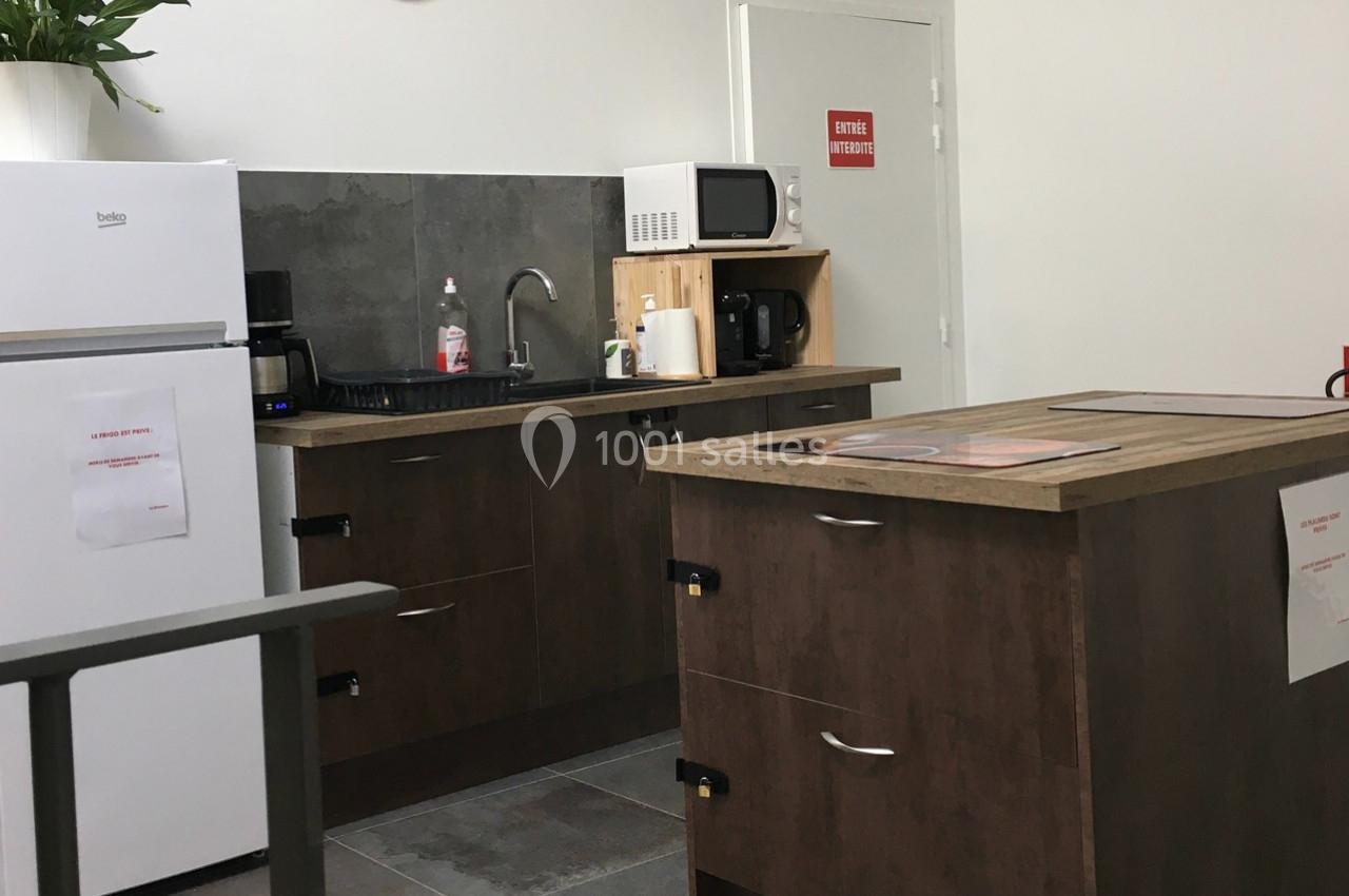 Cuisine équipée avec réfrigérateur, micro-ondes, cafetière, évier et plan de travail en bois, décor sobre et fonctionnel.