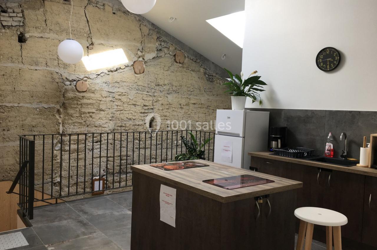 Cuisine moderne avec îlot central, mur en pierre apparente, plafond incliné et éclairage naturel par une fenêtre de toit.