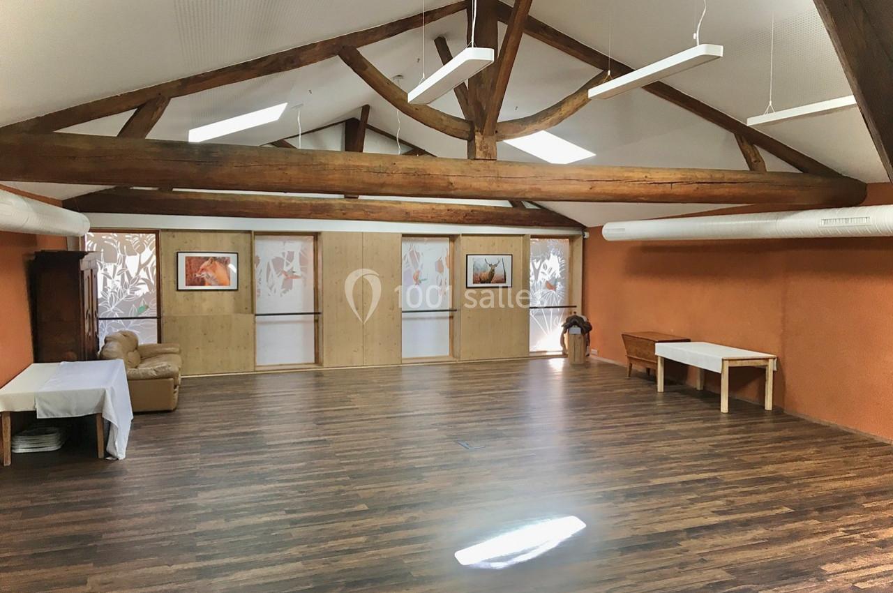 Salle spacieuse avec parquet, murs orange, poutres apparentes et mobilier minimaliste, éclairée par des fenêtres et des…