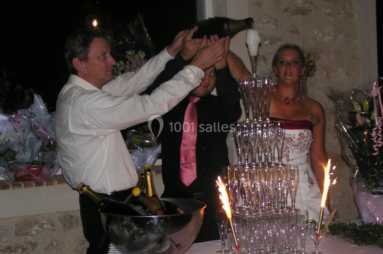 Un homme verse du champagne dans une pyramide de verres lors d'une réception, avec des invités en arrière-plan.