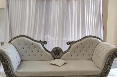 Canapé doré avec assise blanche devant un décor floral et un rideau blanc, éclairé par des appliques murales.