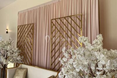 Canapé doré avec assise blanche devant un décor floral et un rideau blanc, éclairé par des appliques murales.