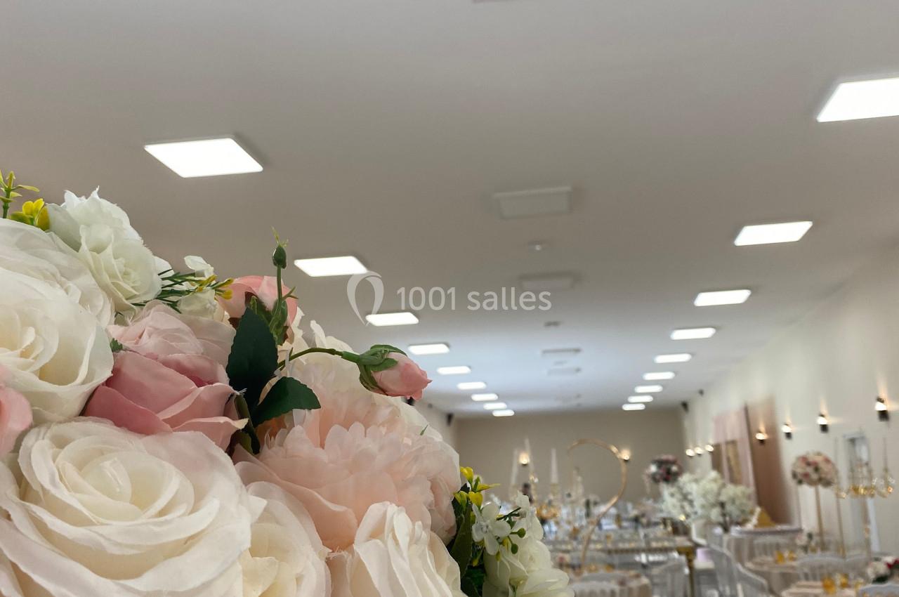 Salle de réception décorée avec des tables dressées et un bouquet de roses blanches et roses au premier plan.