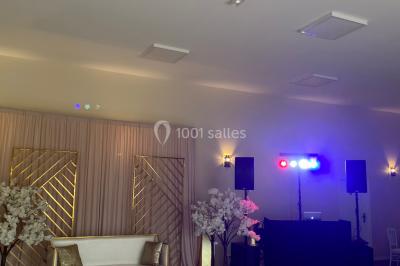 Canapé doré avec assise blanche devant un décor floral et un rideau blanc, éclairé par des appliques murales.