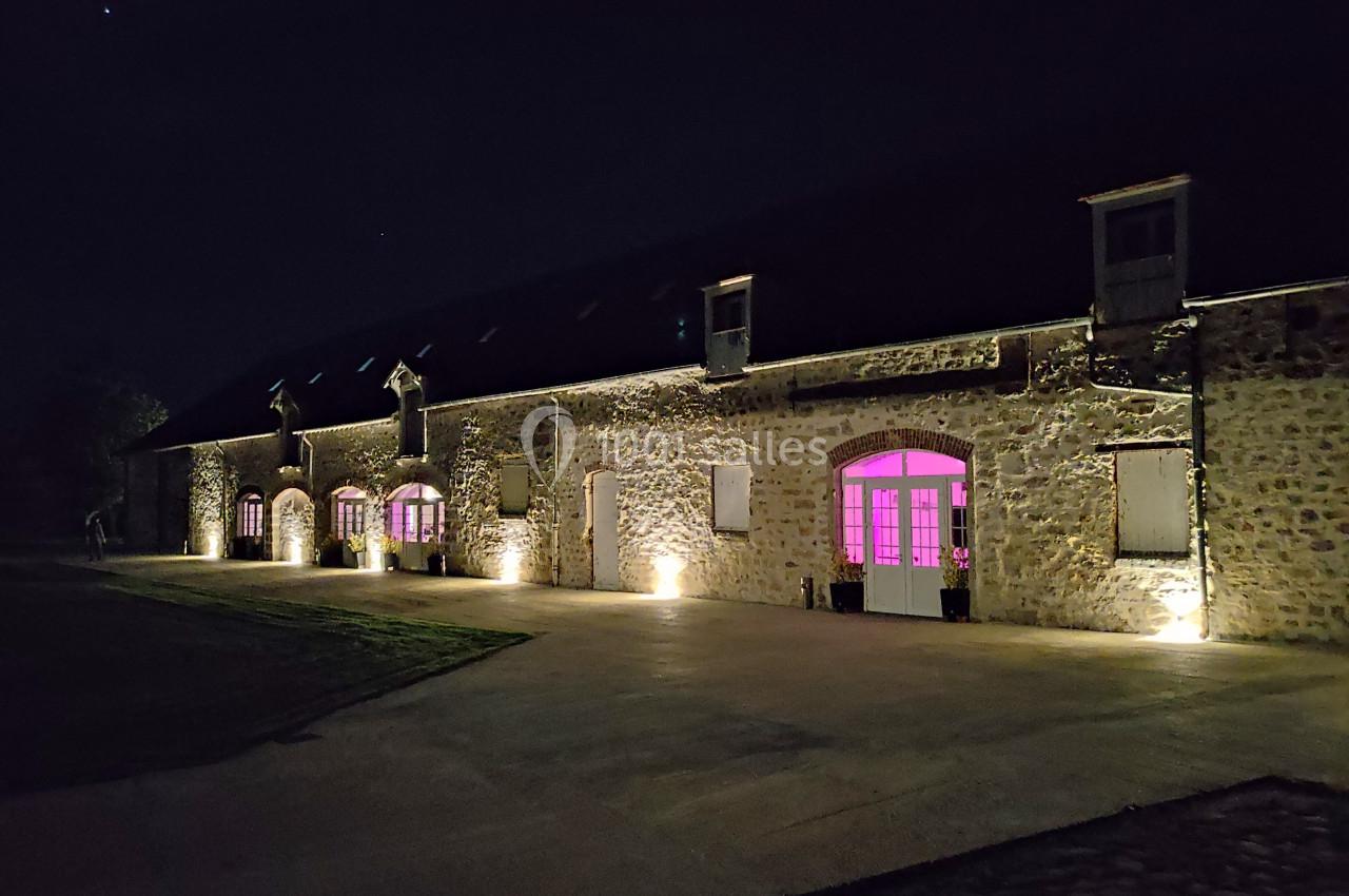Façade en pierre d'un bâtiment éclairé la nuit, avec des fenêtres illuminées en rose.