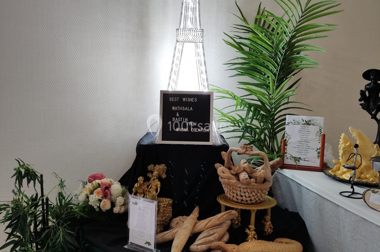 Table décorative avec des pains en forme de baguettes, une tour Eiffel lumineuse et des plantes en arrière-plan.