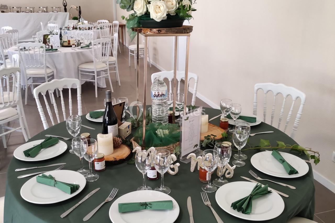 Table de réception décorée avec une nappe verte, vaisselle blanche, centre de table floral et accessoires festifs.