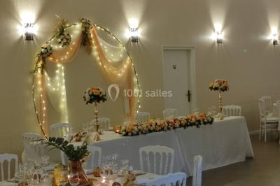 Canapé doré avec assise blanche devant un décor floral et un rideau blanc, éclairé par des appliques murales.