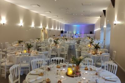 Canapé doré avec assise blanche devant un décor floral et un rideau blanc, éclairé par des appliques murales.