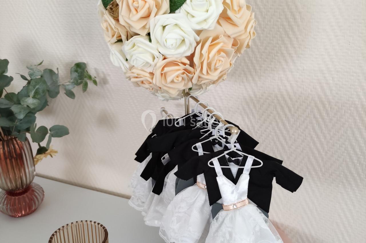 Bouquet de roses crème et pêche sur un support doré, entouré de petites robes blanches suspendues.