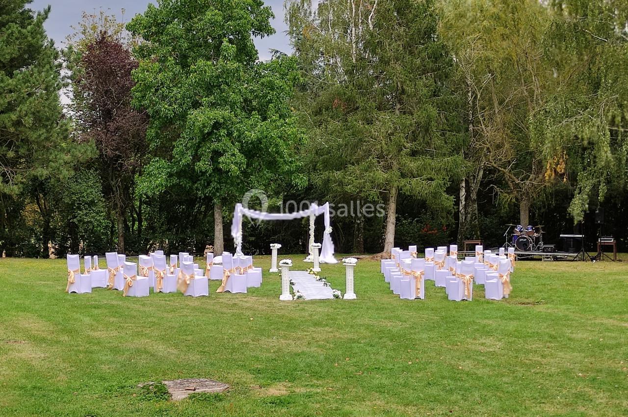 Chaises blanches alignées autour d'une allée centrale menant à une arche décorée, dans un jardin verdoyant.