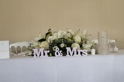 Canapé doré avec assise blanche devant un décor floral et un rideau blanc, éclairé par des appliques murales.