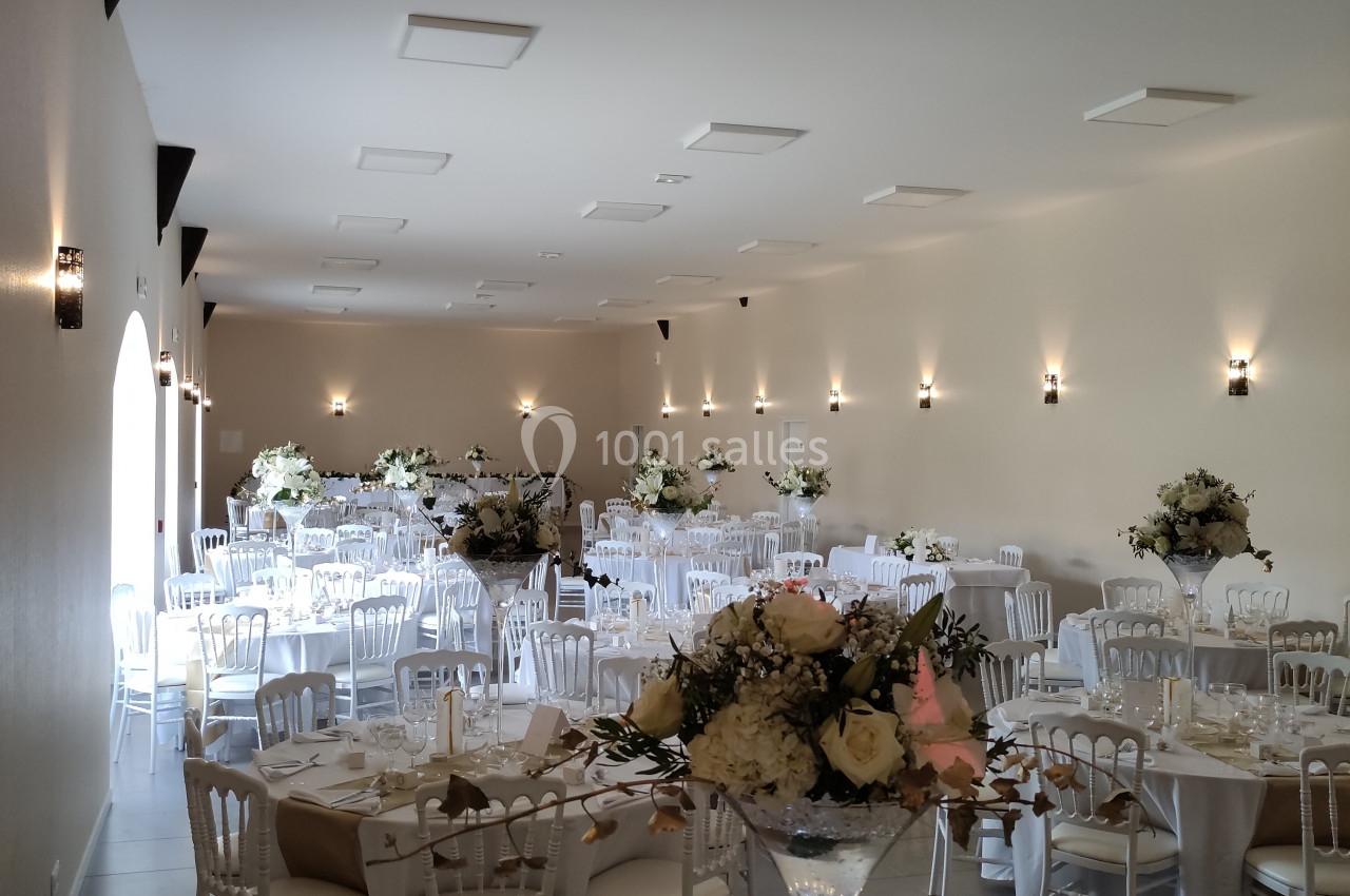 Salle de réception élégamment décorée avec des tables rondes, des nappes blanches et des arrangements floraux.