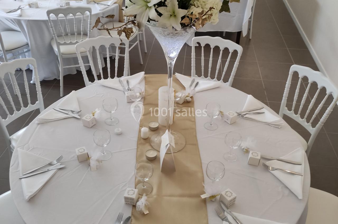 Salle de réception avec tables rondes décorées de nappes blanches, chemins de table dorés et centres de table fleuris.