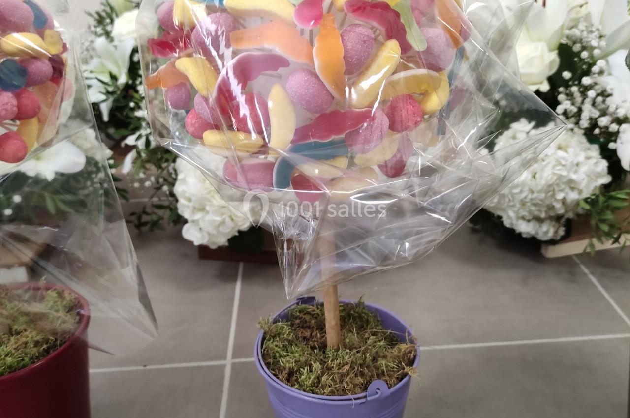 Arbre décoratif en bonbons colorés dans un pot violet, entouré de fleurs blanches en arrière-plan.