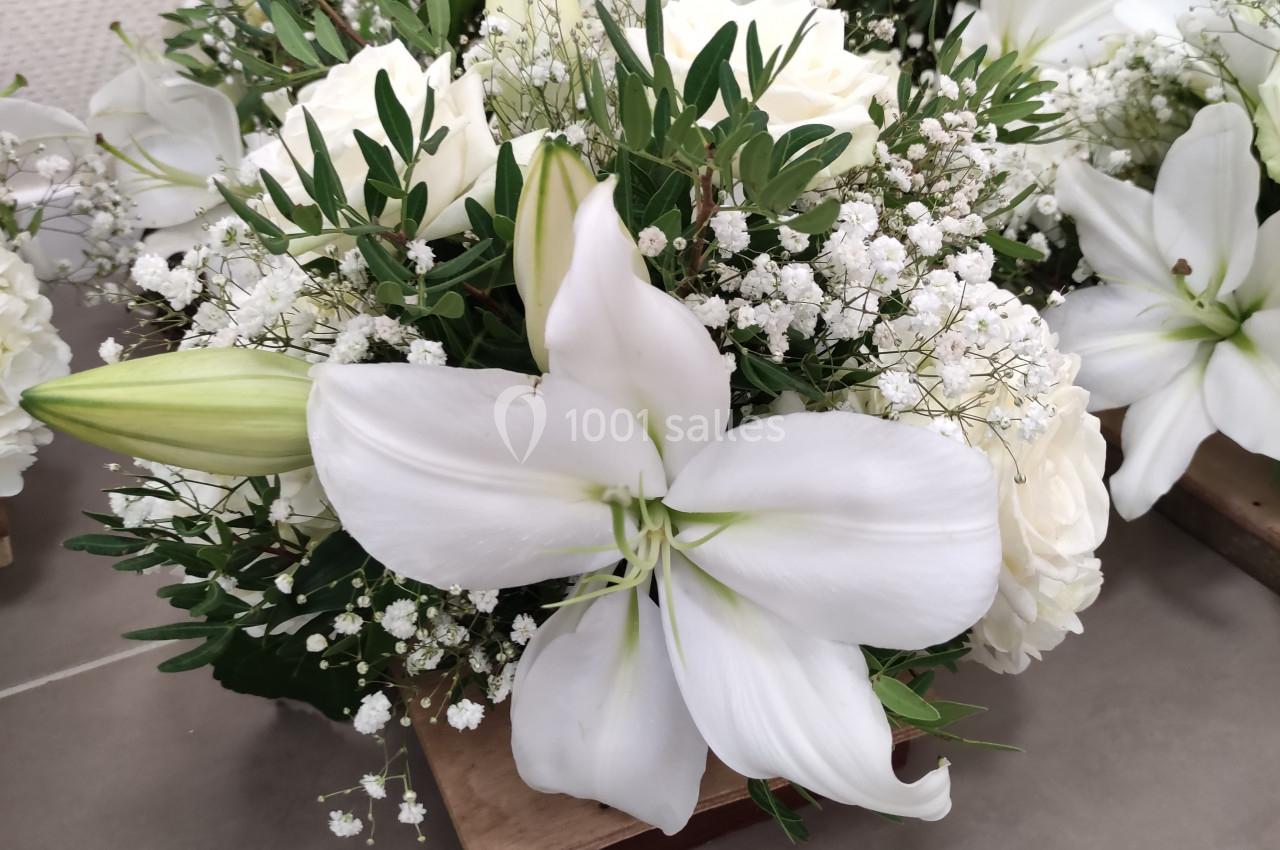 Bouquet de fleurs blanches composé de lys, roses et gypsophiles, posé sur un sol carrelé.