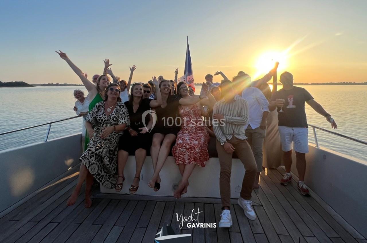 Un groupe de personnes souriantes posant sur le pont d'un bateau au coucher du soleil.