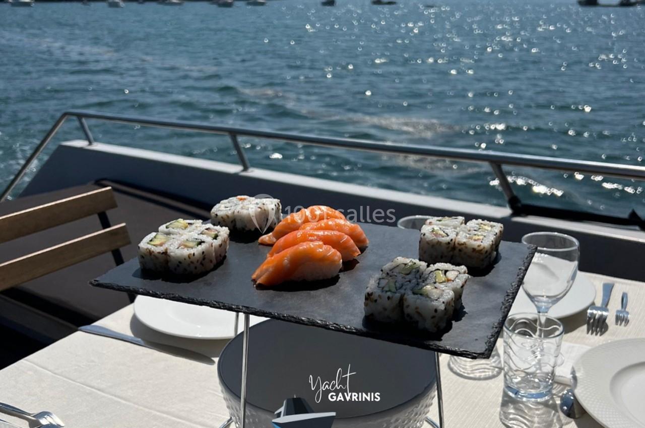 Plateau de sushis et makis sur ardoise, posé sur une table dressée à bord d’un bateau avec vue sur la mer.