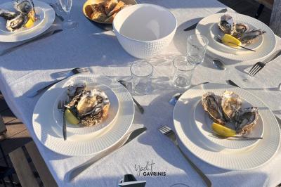 Un homme souriant assis à une table garnie de desserts, sur un bateau avec vue sur la mer et un voilier au loin.