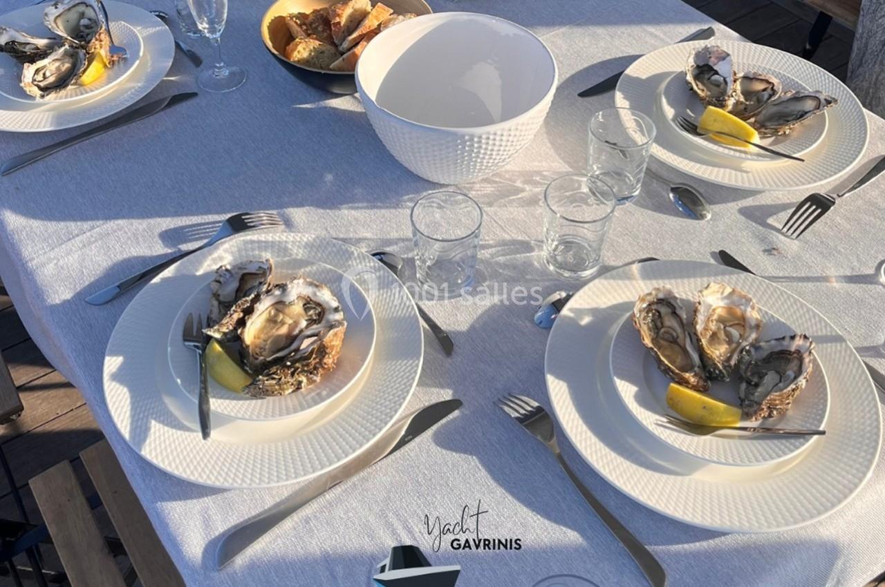Table dressée avec des assiettes d'huîtres, quartiers de citron, couverts et verres sur une nappe blanche.
