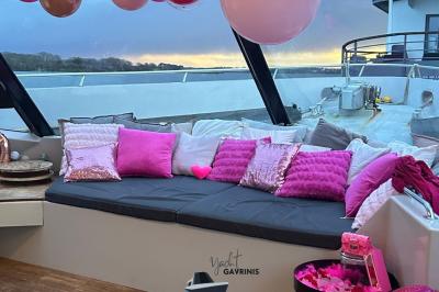 Mobilier en rotin noir avec coussins blancs sur une terrasse en bois couverte, vue sur l'extérieur urbain.