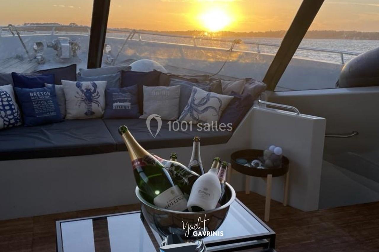 Salon extérieur d'un yacht au coucher du soleil, avec un seau de bouteilles de champagne sur une table basse.