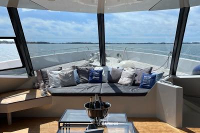 Mobilier en rotin noir avec coussins blancs sur une terrasse en bois couverte, vue sur l'extérieur urbain.