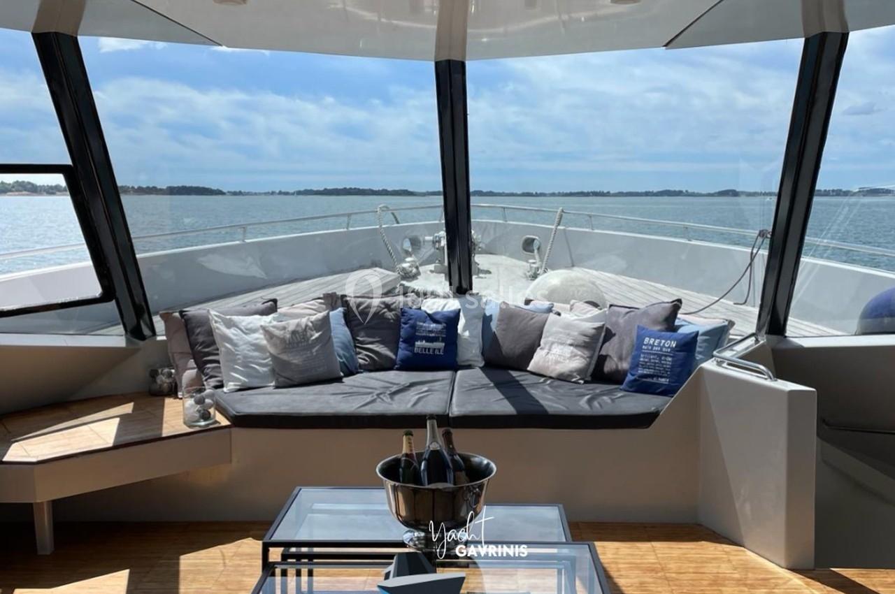 Salon extérieur d'un yacht avec banquette garnie de coussins, table basse et vue sur la mer sous un ciel dégagé.