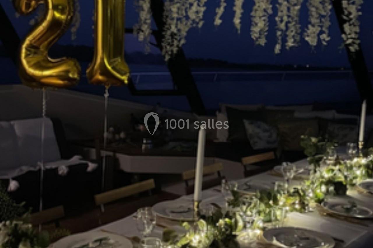 Table élégamment décorée avec guirlandes lumineuses, ballons dorés ’21’ et fleurs suspendues, en soirée.