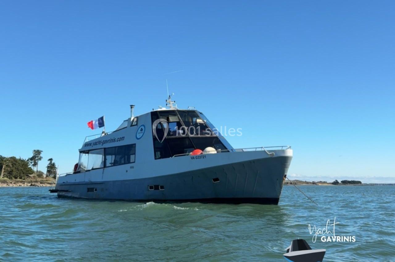 Bateau moderne naviguant sur une eau calme, arborant un drapeau français et un logo sur sa coque.