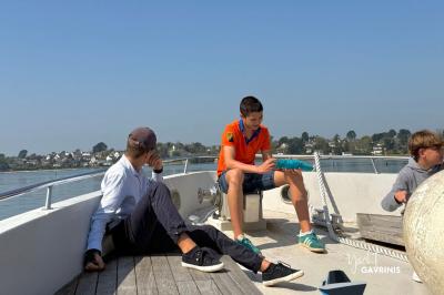 Mobilier en rotin noir avec coussins blancs sur une terrasse en bois couverte, vue sur l'extérieur urbain.