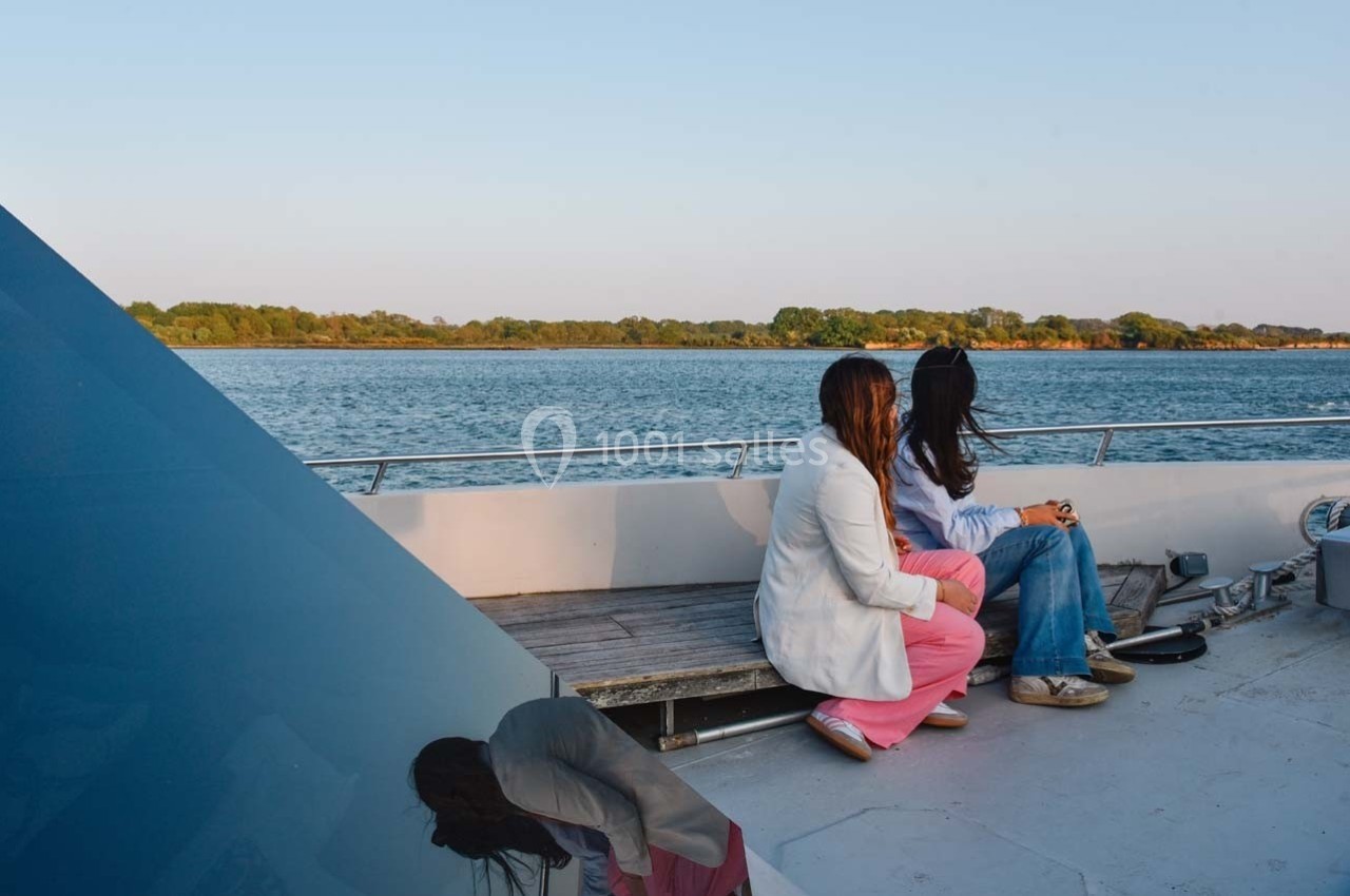 Deux femmes assises sur un banc d'un bateau, regardant un paysage de rivière bordé de végétation.