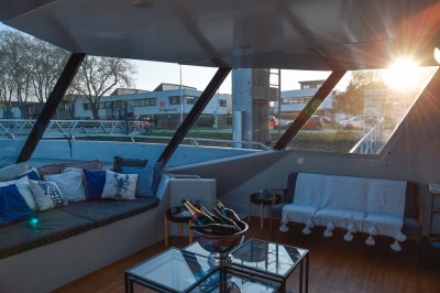 Mobilier en rotin noir avec coussins blancs sur une terrasse en bois couverte, vue sur l'extérieur urbain.