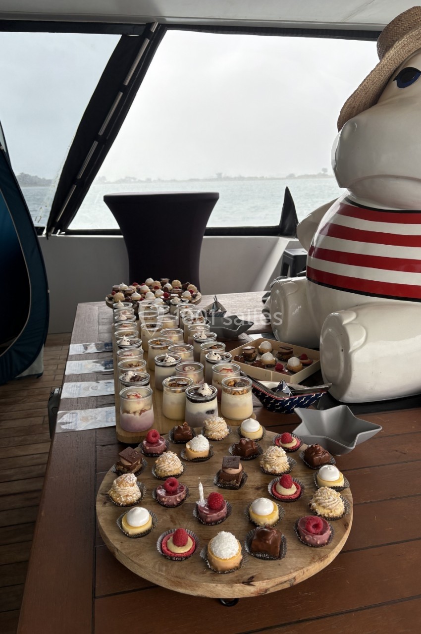 Plateaux de desserts variés disposés sur une table en bois, avec une vue sur la mer en arrière-plan.