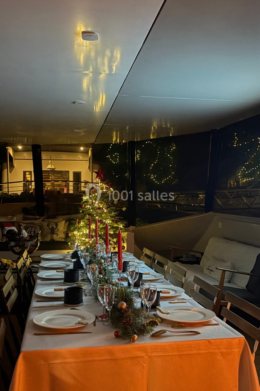 Table dressée pour un repas festif avec bougies rouges, décorations de Noël et sapin illuminé en arrière-plan.