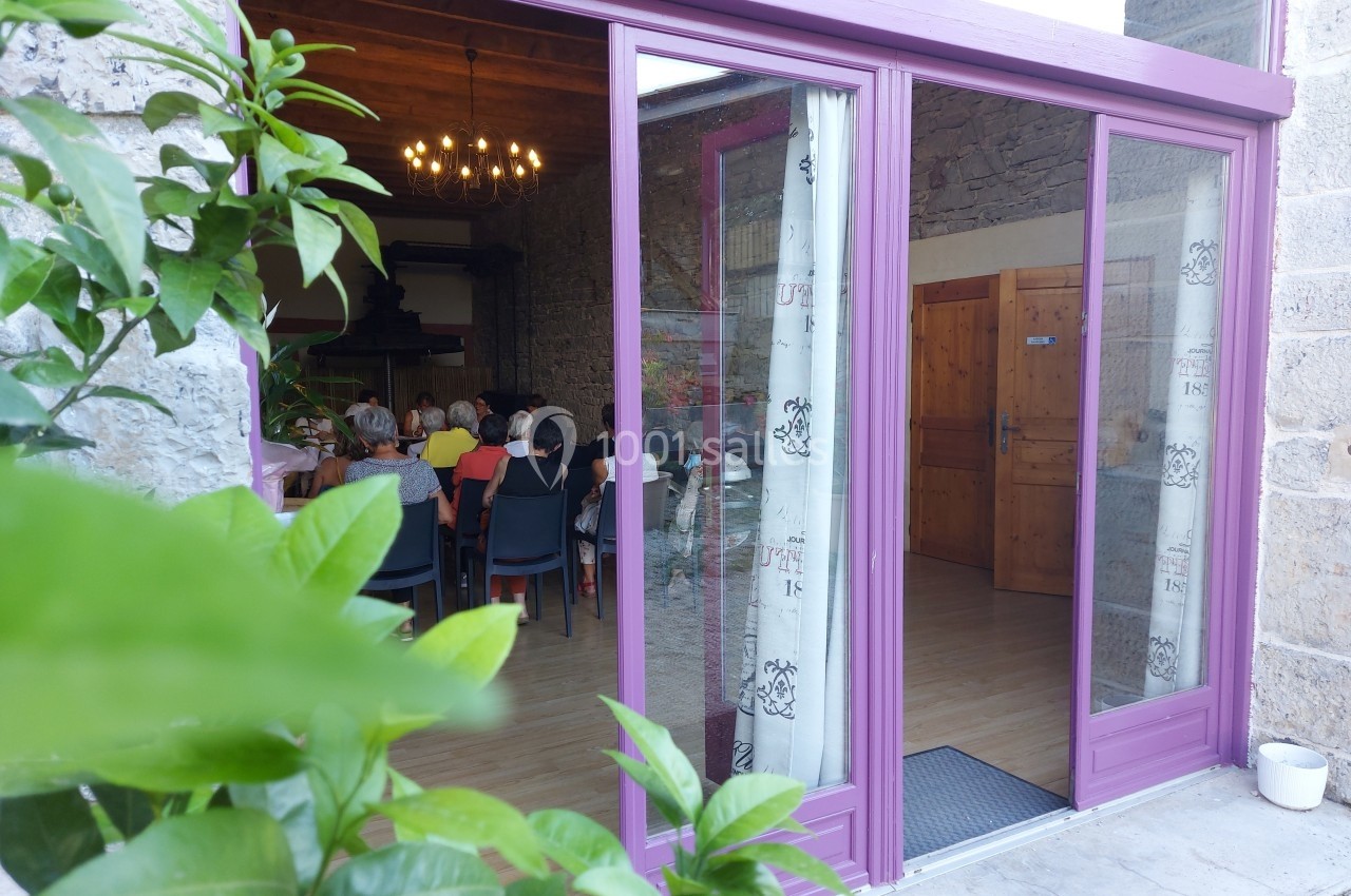 Vue d'une salle de réunion à travers une baie vitrée ouverte, avec des personnes assises autour de tables.
