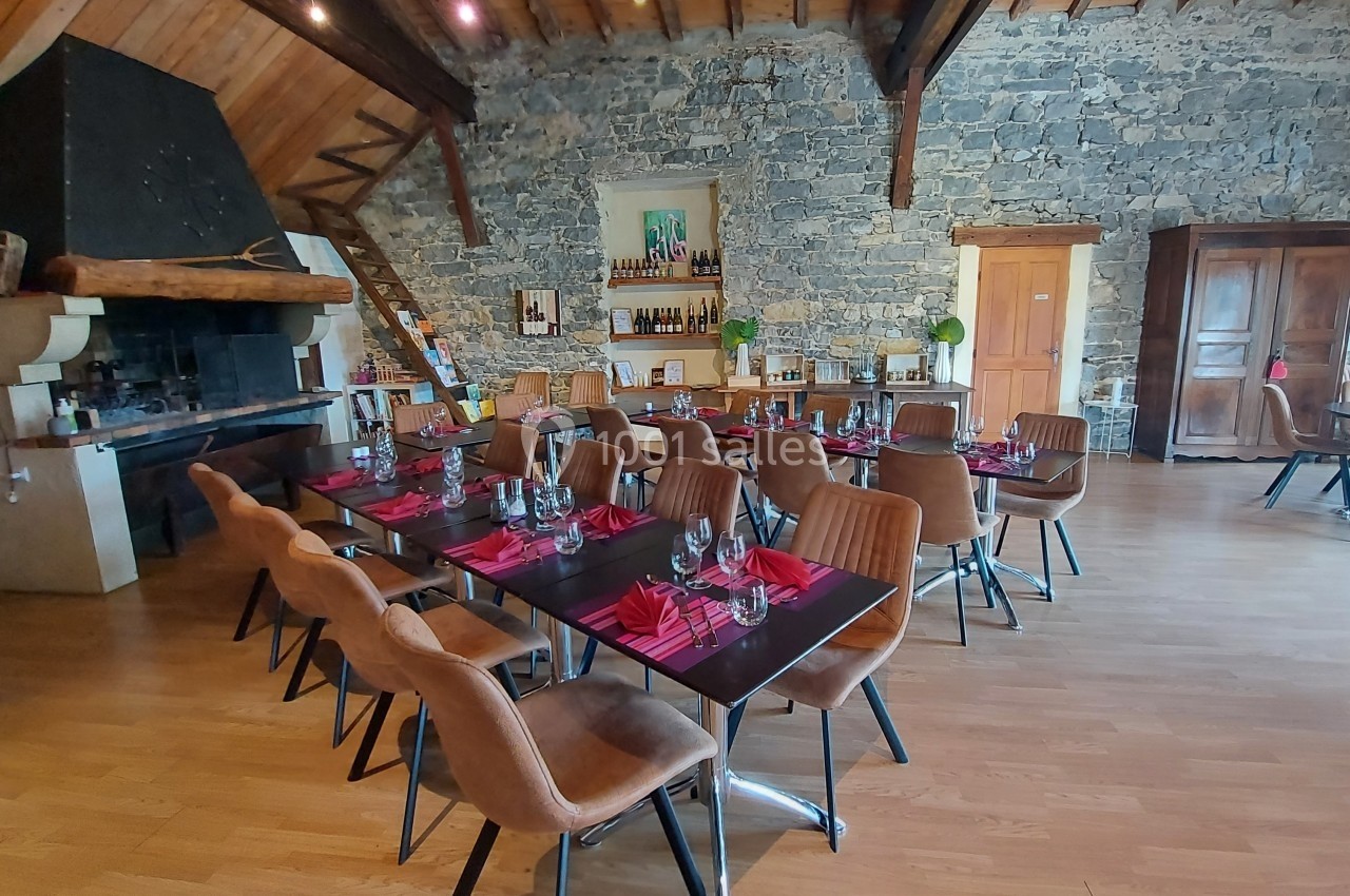 Salle de restaurant avec tables dressées, chaises en cuir, murs en pierre et cheminée rustique.